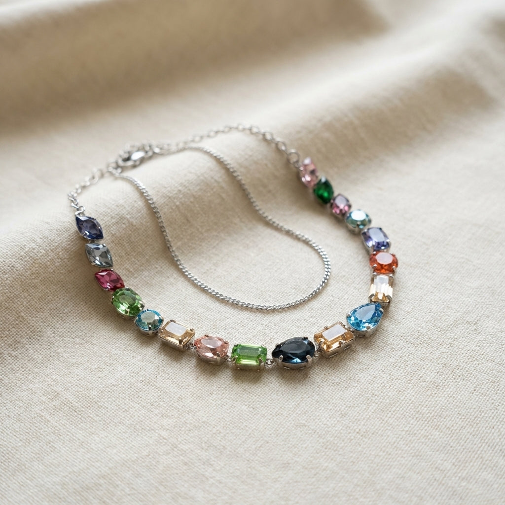 Flat lay of miniature multicolour Swarovski necklace with accessories, showcasing fine craftsmanship and vibrant stones on textured surface.
