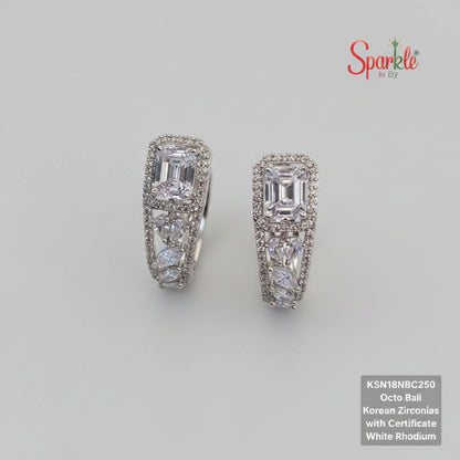 Pair of diamond earrings on a beige surface with a green fabric background, featuring the brand 'SparkebyDJ'.