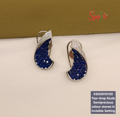 Tear-drop shaped stud earrings with blue stones and silver accents on a beige surface, branded 'SparklebyDJ'.