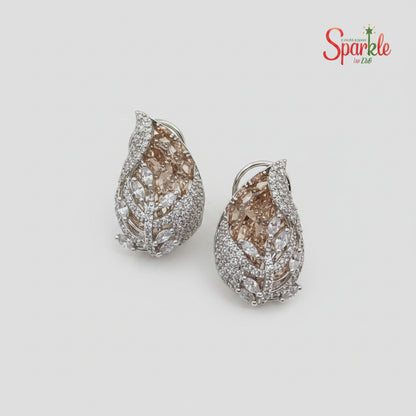 Pair of pear-shaped champaigne earrings with white rhodium finish on a beige background, branded 'SparklebyDJ"