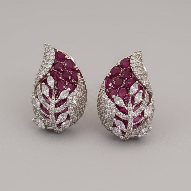 Pear-shaped 3D earrings with red gemstones and white rhodium on a beige background, branded 'SparklebyDJ'.