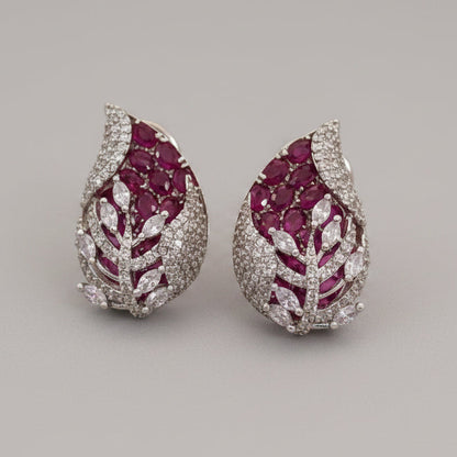 Pear-shaped 3D earrings with red gemstones and white rhodium on a beige background, branded 'SparklebyDJ'.
