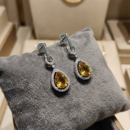 Close-up of a petite CZ drop earring on textured velvet cushion, showcasing micro craftsmanship, pear-shaped stone, in gentle lighting.