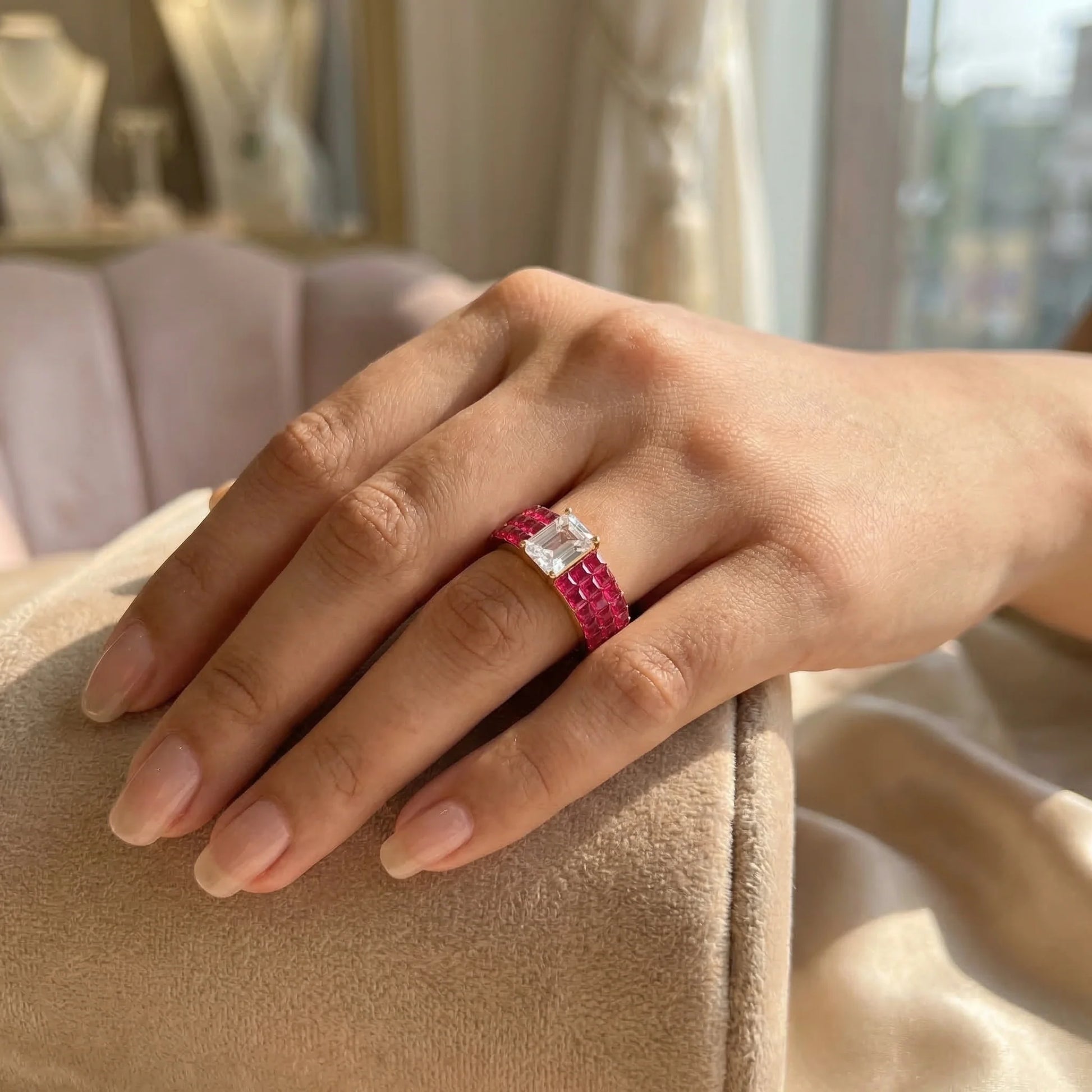 Hand wearing a red and silver ring on a beige surface with a blurred indoor background